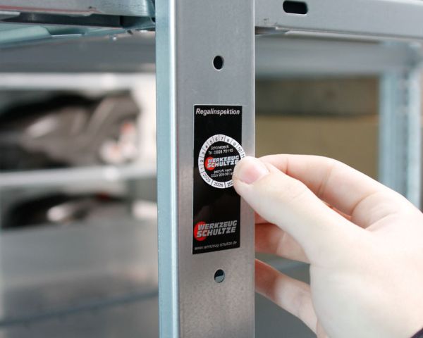 Plakette zur Regalinspektion wird an Metallregal angebracht – dokumentierte Prüfung für sichere und vorschriftskonforme Lagertechnik.