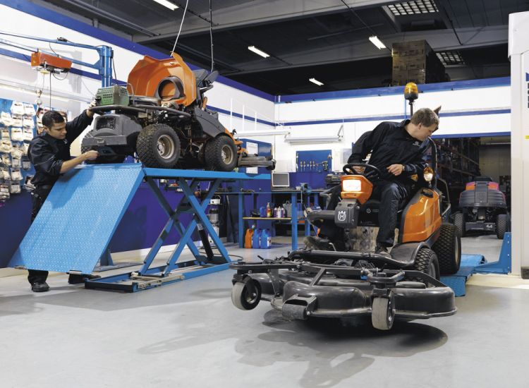 Servicearbeiten an Aufsitzmähern in der Werkstatt – Techniker warten und prüfen Mähdecks auf Hebebühnen.