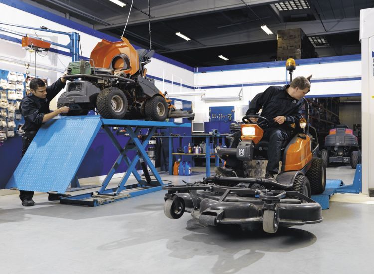 Servicearbeiten an Aufsitzmähern in der Werkstatt – Techniker warten und prüfen Mähdecks auf Hebebühnen.