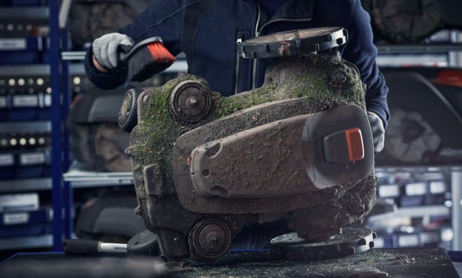 Reinigung und Wartung eines Mähroboters in der Werkstatt – Techniker entfernt Grasreste und Schmutz vom Gehäuse.